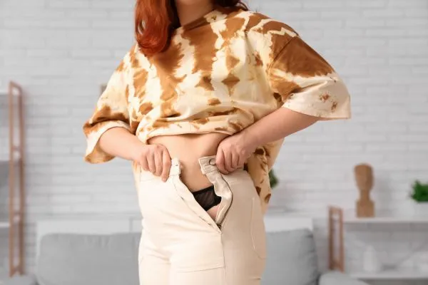 Image of woman trying to do her trousers up after pregnancy weight gain Basildon