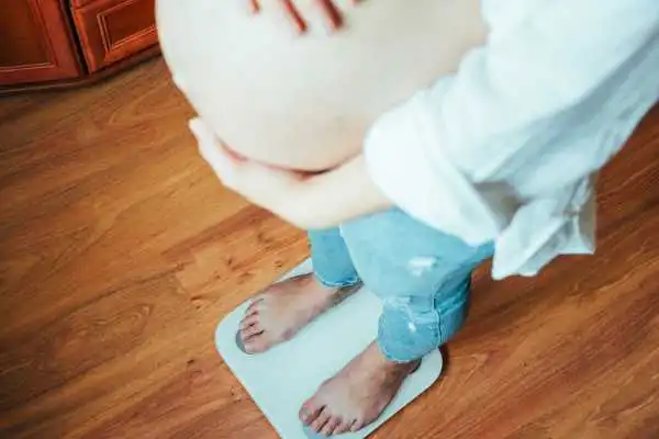 Image of woman weighing herself and experiencing weight gain through pregnancy Basildon